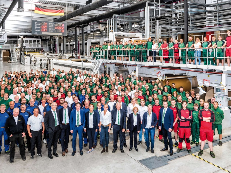 Gruppenfoto in der Halle der Wellpappenanlage mit über 100 Mitarbeiterinnen und Mitarbeitern, Azubis und der Geschäftsleitung